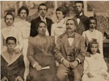 Fotografía antigua en blanco y negro de una familia numerosa; los hombres visten traje y las mujeres vestidos largos, lo que ilustra roles de género tradicionales.