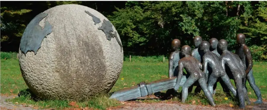 Escultura de un grupo de figuras humanas empujando con una palanca una gran esfera de piedra con formas de continentes, símbolo de trabajo comunitario.
