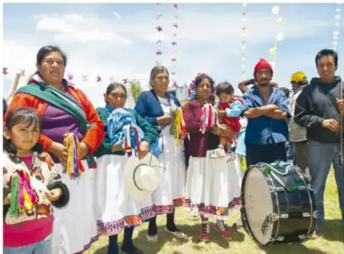 Fotografía de un grupo de mujeres otomíes con vestimenta tradicional, artesanías y un tambor, en una celebración al aire libre.