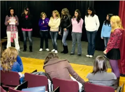 Fotografía de un grupo de estudiantes presentando sobre un escenario ante un público sentado en sillas.