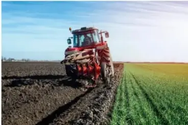 Fotografía de una cosechadora o tractor moderno trabajando en un gran campo sembrado, representando la agricultura intensiva o mecanizada.