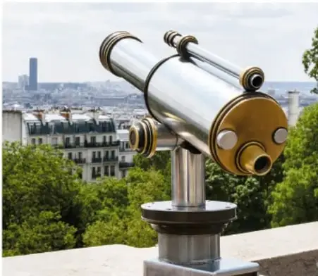 Fotografía de un telescopio óptico moderno montado sobre una base, con una ciudad al fondo.