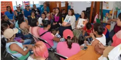 Reunión comunitaria con personas adultas y jóvenes sentadas alrededor de mesas, en un espacio de participación.