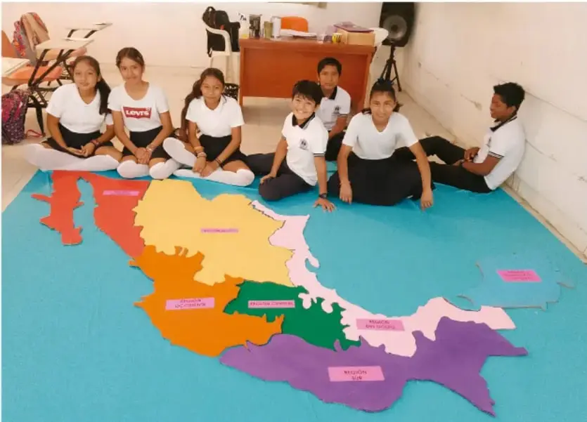 Fotografía de estudiantes de Telesecundaria sentados en el piso alrededor de un mapa de México elaborado en cartón con las regiones señaladas por colores.