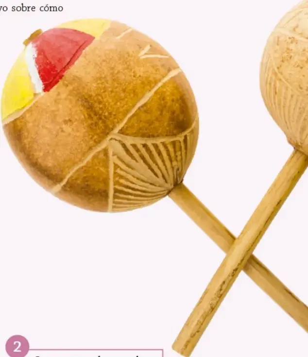 Fotografía de dos maracas (maraquitas) artesanales de madera con diseños tallados y pintados en rojo y amarillo, con mangos largos cruzados.