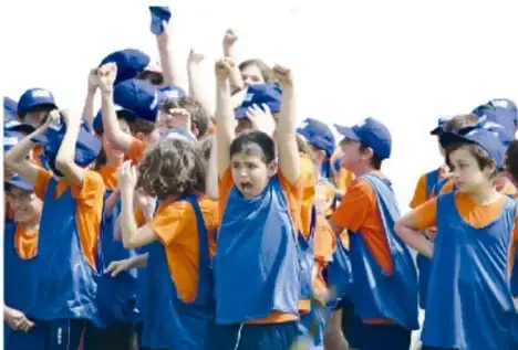 Grupo de niños y niñas con playeras azules y naranjas, con los brazos en alto, celebrando y aplaudiendo.