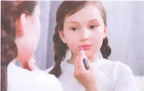 Fotografía de una niña observándose en un espejo mientras se aplica maquillaje.