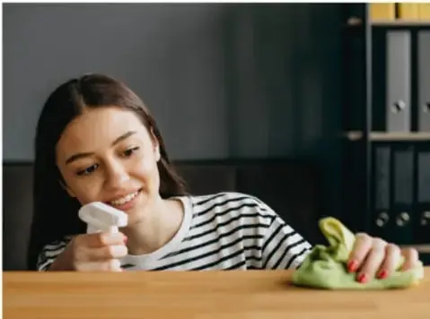 Joven o niña limpiando una mesa con un paño, colaborando con las tareas del hogar.