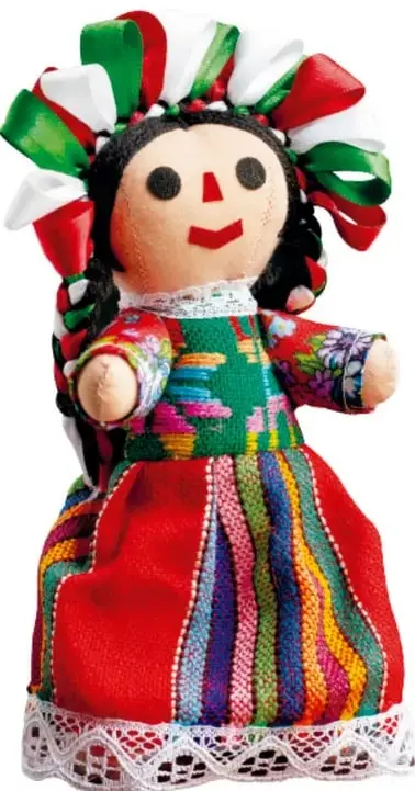 Muñeca Lele de gran tamaño con listones verdes, blancos y rojos en la cabeza, blusa bordada multicolor y falda roja con franjas de colores.