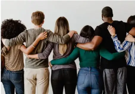 Grupo de jóvenes diversos de espaldas, abrazados, simbolizando inclusión y unidad.