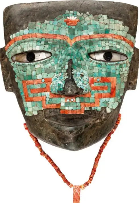Máscara funeraria decorada con mosaicos de turquesa y conchas rojas, con ojos de concha y collar de cuentas rojas.