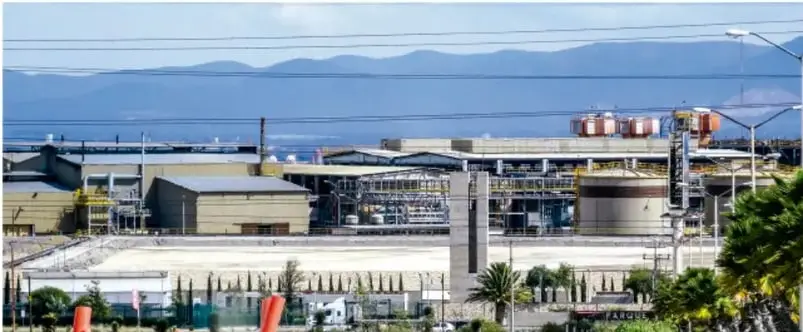 Fotografía de una planta industrial con tanques, estructuras metálicas y montañas al fondo, junto a palmeras y camellones; representa el contexto socioeconómico analizado en el proyecto académico.