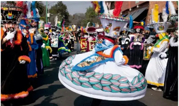 Fotografía de un desfile o comparsa de personas con vestimenta tradicional mexicana colorida, incluyendo grandes sombreros y trajes decorados; crédito Corbis-Hulton / Ciudad de México