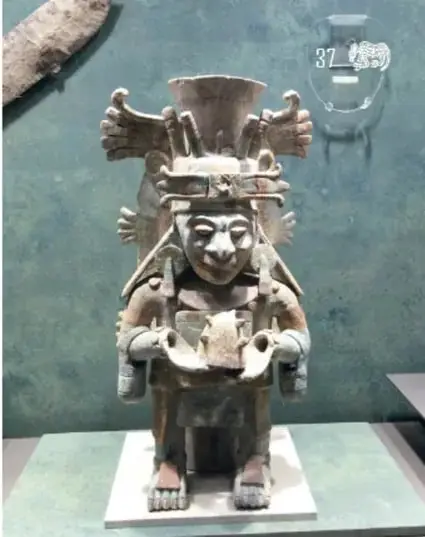 Fotografía de una pieza arqueológica antropomorfa con tocado, exhibida en una vitrina del museo.