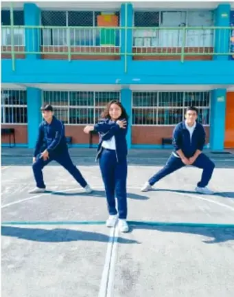 Fotografía de tres estudiantes (dos hombres y una mujer) en actitud deportiva sobre una cancha escolar, ilustrando la vida saludable.