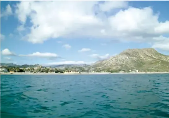 Vista panorámica de Cabo Pulmo: mar azul, cielo con nubes y cerros áridos al fondo.
