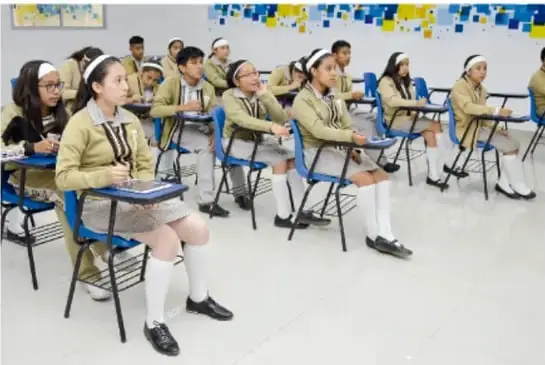 Fotografía de un grupo de estudiantes en un aula, sentados en sus pupitres, con uniforme escolar.