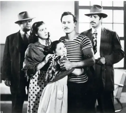 Fotografía en blanco y negro de una escena cinematográfica con cinco personas: dos hombres con sombrero, una mujer con rebozo, un hombre con camiseta rayada y una niña.
