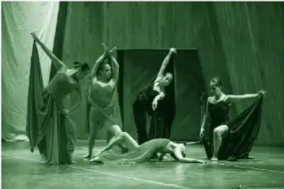 Fotografía a color (en tinta verde del libro) de cinco bailarinas de danza contemporánea en un escenario: una sentada sobre el suelo y cuatro formando un semicírculo con brazos extendidos, vestidos largos, tres rojos y dos negros, pies descalzos y cabello recogido.