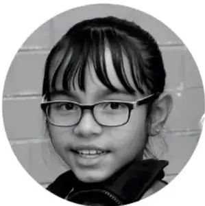Fotografía de una niña con lentes y suéter oscuro, sonriendo.