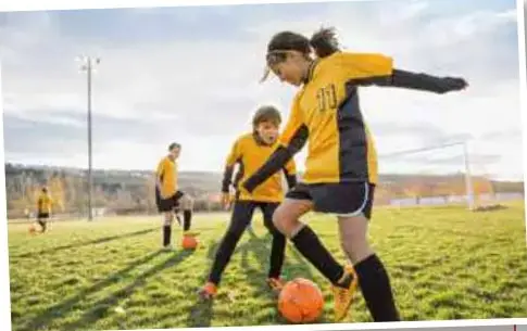 Niños jugando fútbol en una cancha de pasto con uniforme amarillo y negro.