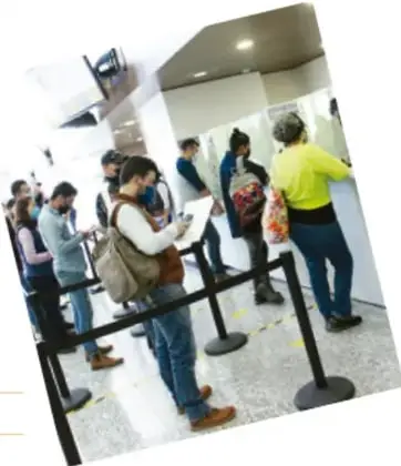 Fotografía de personas formadas en una oficina pública, esperando ser atendidas para realizar un trámite.