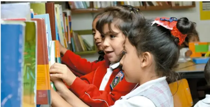 Fotografía de niñas de primaria revisando libros en la biblioteca de aula, ilustrando la actividad de investigación de la Biblioteca de Aula.