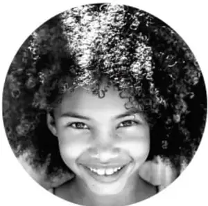 Fotografía circular en blanco y negro de una niña sonriente con cabello rizado abundante.