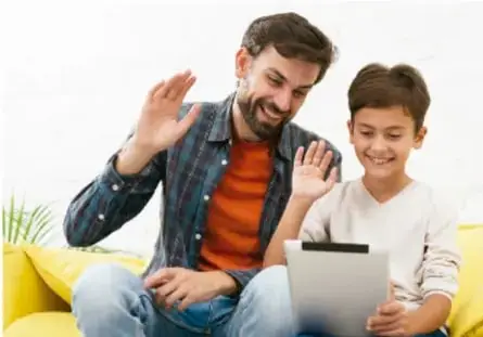 Fotografía de un adulto y un niño sentados en un sillón amarillo usando una tableta, con gestos de sorpresa y alegría.
