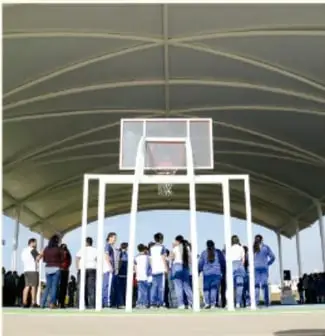 Estudiantes reunidos en una cancha deportiva techada con un tablero de básquetbol al fondo.