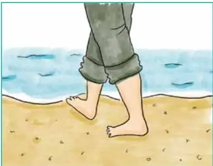 Piernas de un niño caminando descalzo sobre la arena de la playa.