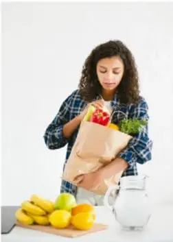 Mujer con bolsa de víveres, frutas (plátanos, limones) y un garrafón de agua, representando una alimentación variada y el consumo de agua potable.