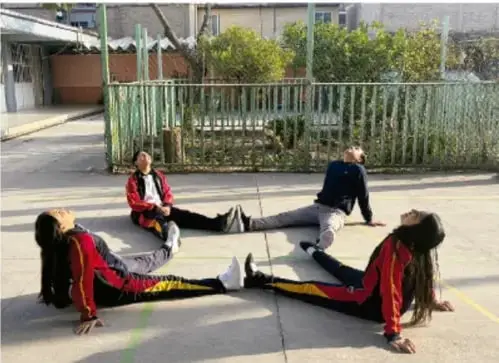 Fotografía de estudiantes sentados en el piso del patio escolar, en círculo, realizando ejercicios de respiración/relajación antes de una presentación.