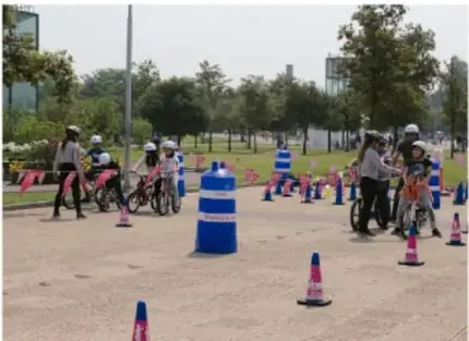 Fotografía de un grupo de personas en bicicleta y con cascos realizando una actividad en un espacio al aire libre con conos.