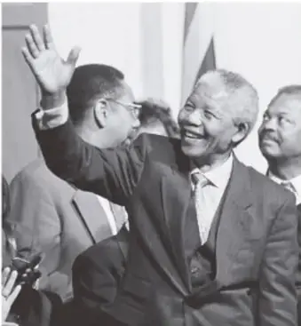 Mandela saludando con la mano, acompañado de otras personas.