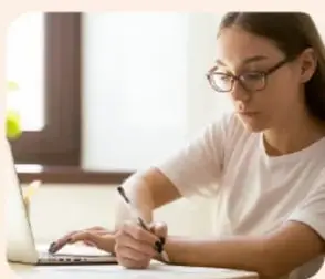 Estudiante con lentes trabajando frente a una computadora portátil, tomando notas, representando el análisis de datos cuantitativos.