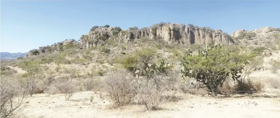 Fotografía panorámica del paisaje rocoso del cerro: formaciones rocosas verticales, nopales, arbustos secos y cielo azul.