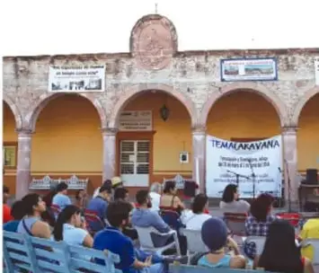 Asamblea comunitaria en un patio con personas sentadas escuchando a un orador.