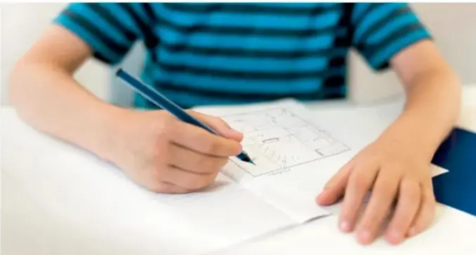 Fotografía de un estudiante de camisa rayada dibujando con lápiz un mapa sobre una mesa blanca