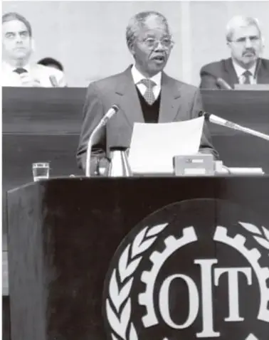 Nelson Mandela hablando en un atril con el emblema de la OIT (Organización Internacional del Trabajo) al fondo.