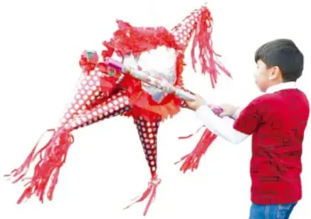Niño con camiseta roja y jeans sosteniendo un muñeco o figura de fiesta con listones rojos y blancos, posiblemente de un desfile o carnaval.