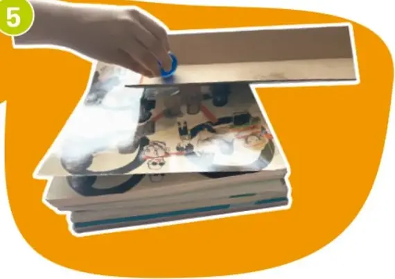 Mano soltando una canica por una rampa inclinada con libros.
