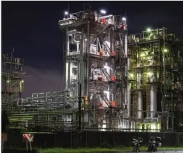 Planta industrial iluminada de noche, con torres y estructuras metálicas, representando la producción que requiere energía.