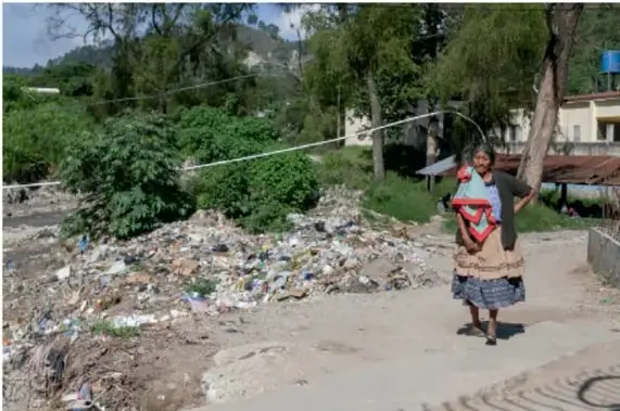 Fotografía de una calle en comunidad rural con basura acumulada a los lados y una persona caminando, ilustrando la contaminación en zonas rurales.