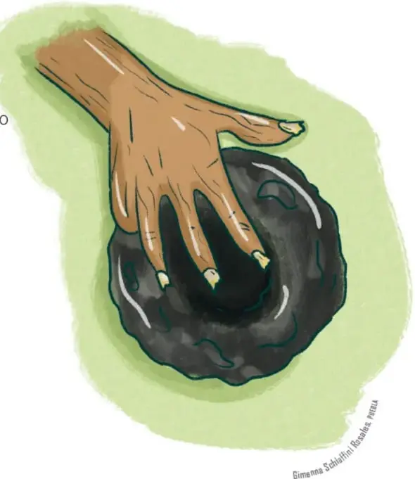 Mano grande que toma un disco circular negro brillante de piedra, el disco de pedernal que la anciana escondió en el cabello del enano.