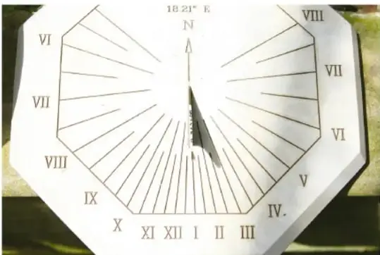 Reloj solar de piedra con una placa radial marcada con números romanos y una gnomon que proyecta la sombra para indicar la hora.