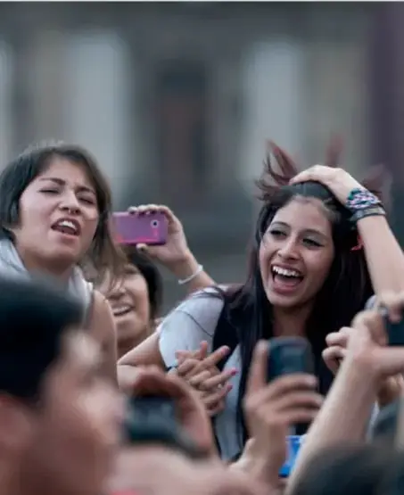 Grupo de jóvenes sonrientes conviviendo en un espacio comunitario, algunos tomando fotos con teléfonos móviles, ilustrando la participación juvenil en la vida comunitaria.