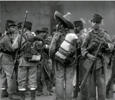 Fotografía en blanco y negro de un grupo de soldados revolucionarios con uniformes y armas, representando la lucha armada de la Revolución Mexicana.