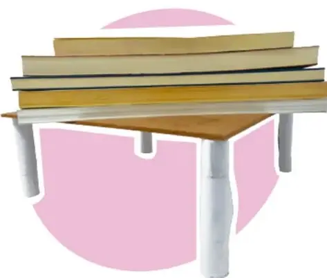 Pila de libros sobre una tabla sostenida por tubos de papel blancos que hacen de columnas, con fondo rosa.
