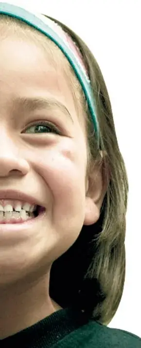 Primer plano de una niña sonriente con diadema verde; su rostro ilustra la simetría bilateral del cuerpo humano.